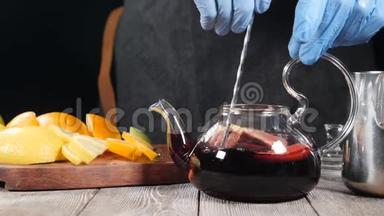 用勺子把热红酒和水果片放在茶壶里搅拌。玻璃茶壶里装满了橘子和柠檬